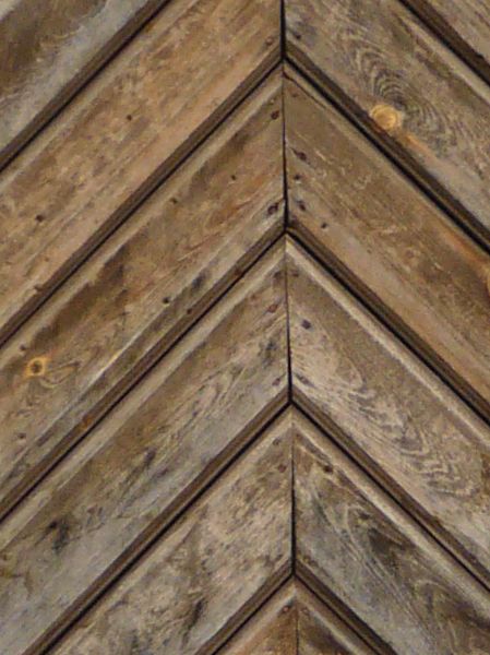 Old wooden door with arching top and diamond pattern on surface.